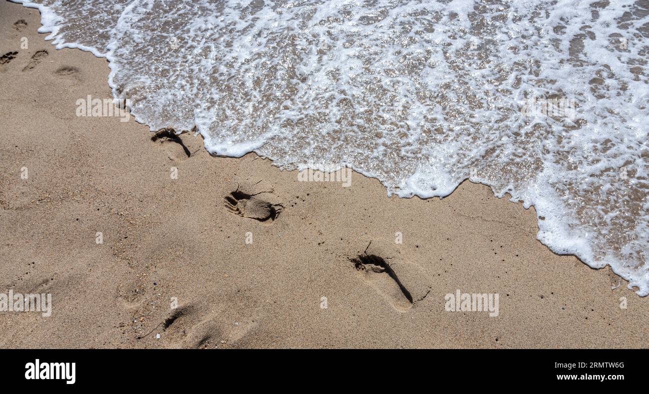 Footprints of a man on the yellow beach sand from walking barefoot by the sea with water that washes away the footprints. Contemplation of life Stock Photo
