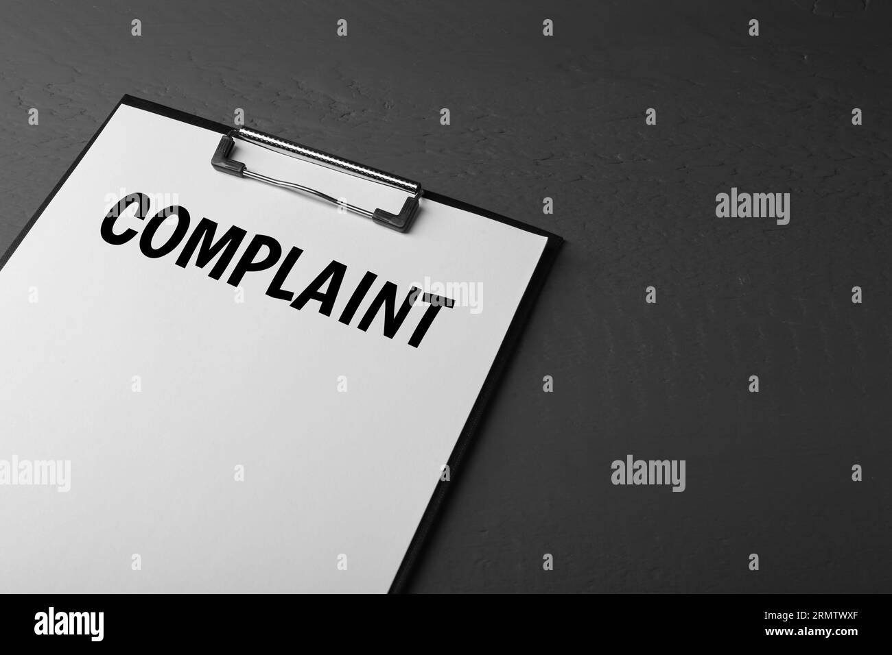 Paper with word Complaints attached to clipboard on black background
