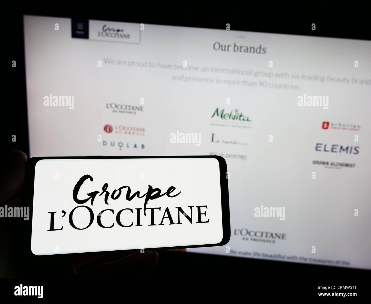 Person holding smartphone with logo of French cosmetics company Groupe L'Occitane on screen in front of website. Focus on phone display. Stock Photo