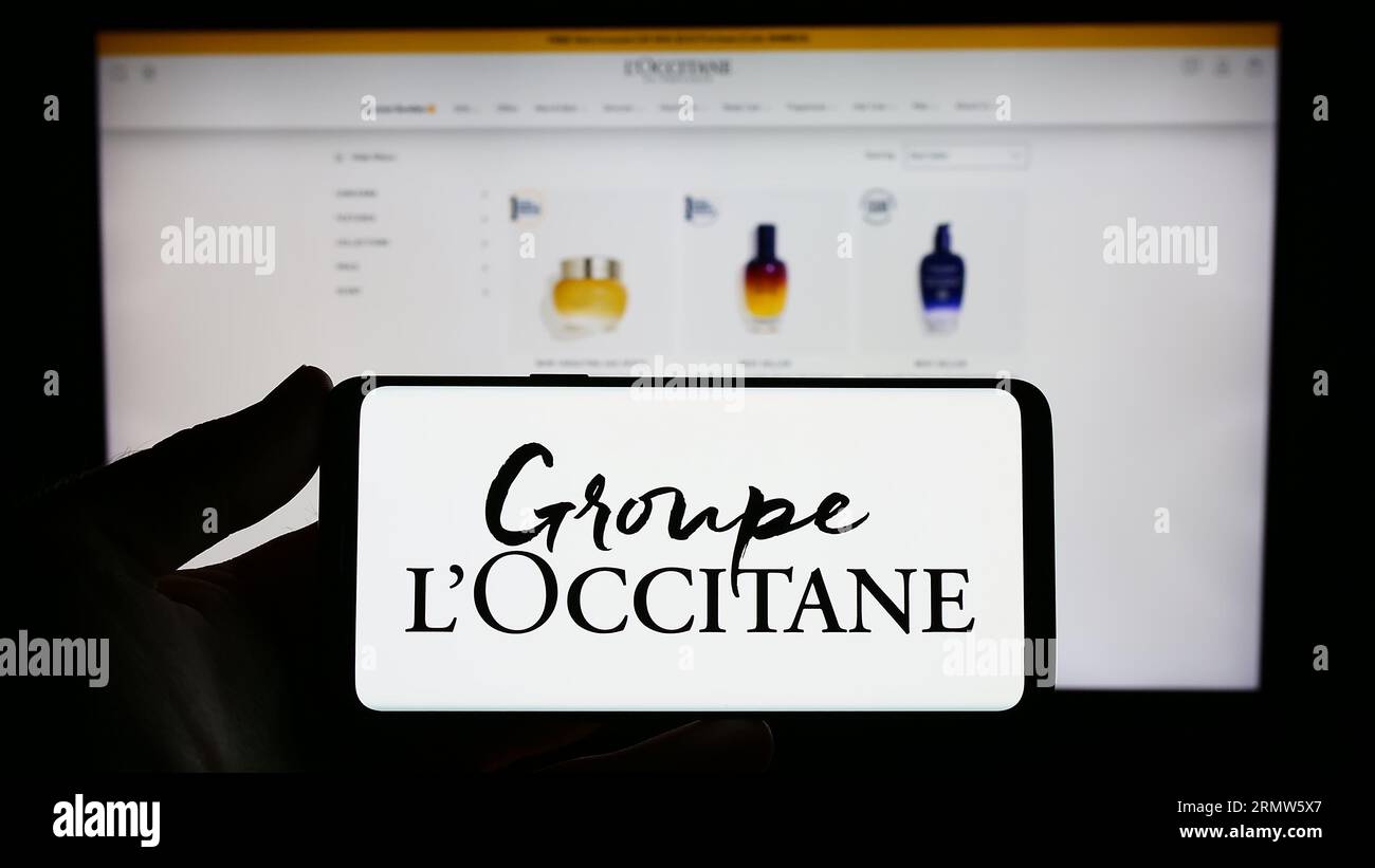 Person holding cellphone with logo of French cosmetics company Groupe L'Occitane on screen in front of business webpage. Focus on phone display. Stock Photo