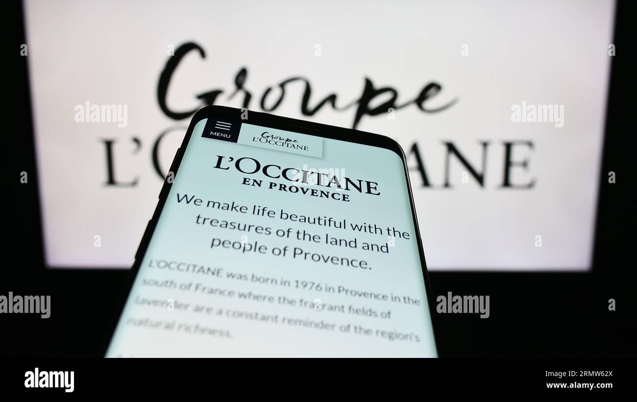 Mobile phone with website of French cosmetics company Groupe L'Occitane on screen in front of business logo. Focus on top-left of phone display. Stock Photo