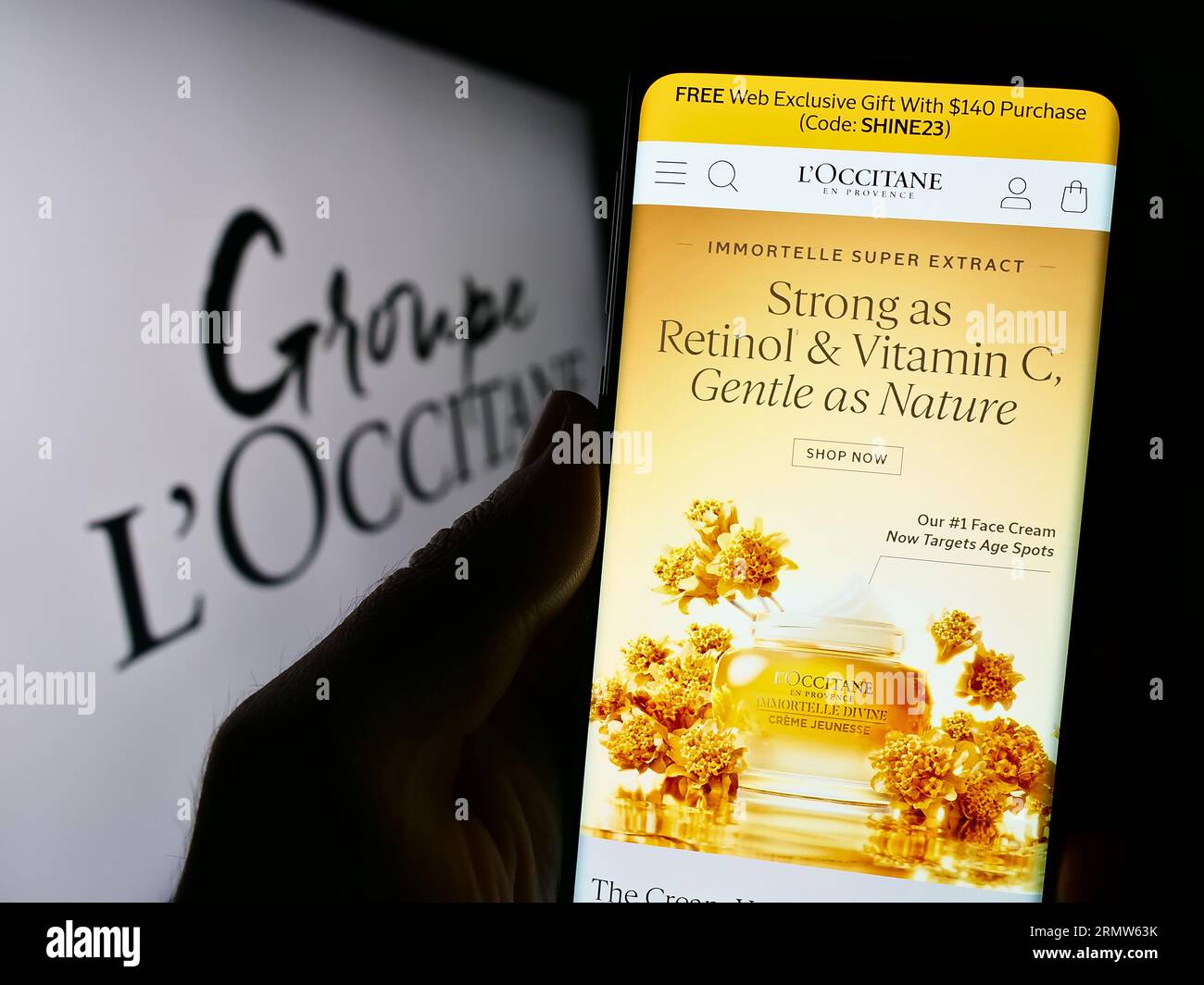 Person holding cellphone with webpage of French cosmetics company Groupe L'Occitane on screen in front of logo. Focus on center of phone display. Stock Photo