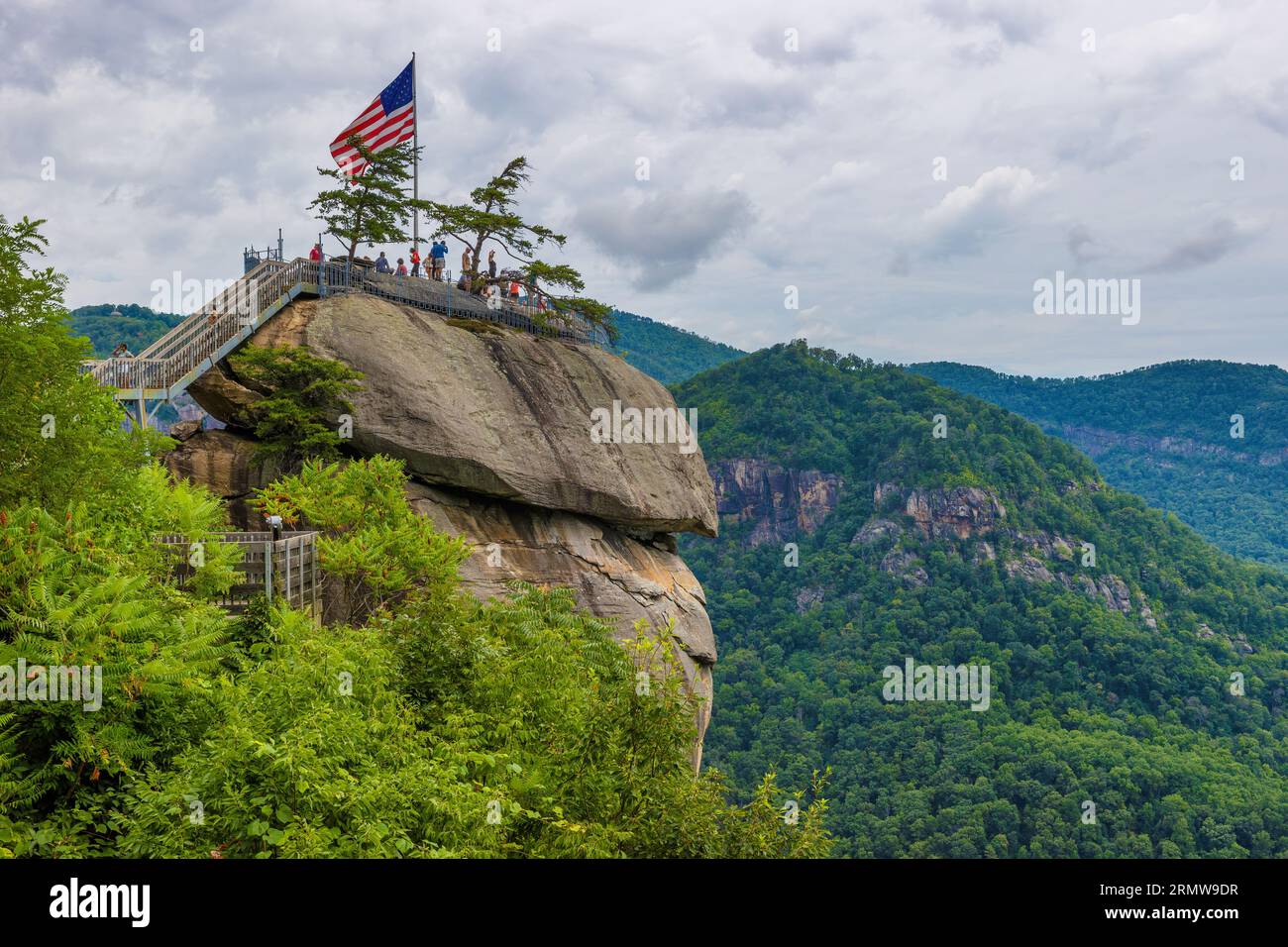 Chimney Rock, North Carolina, USA - August 11, 2023: view above of the top of Chimney Rock where the American Flag flies and people climb stairs to se Stock Photo