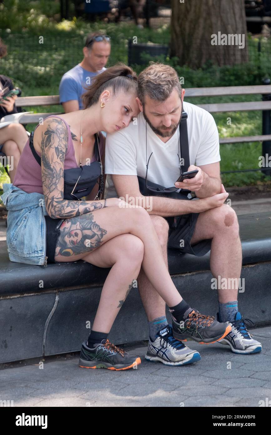 A weary French couple pause to rest and check a cell phone on a bench in Washington Square Park in Manhattan. Stock Photo