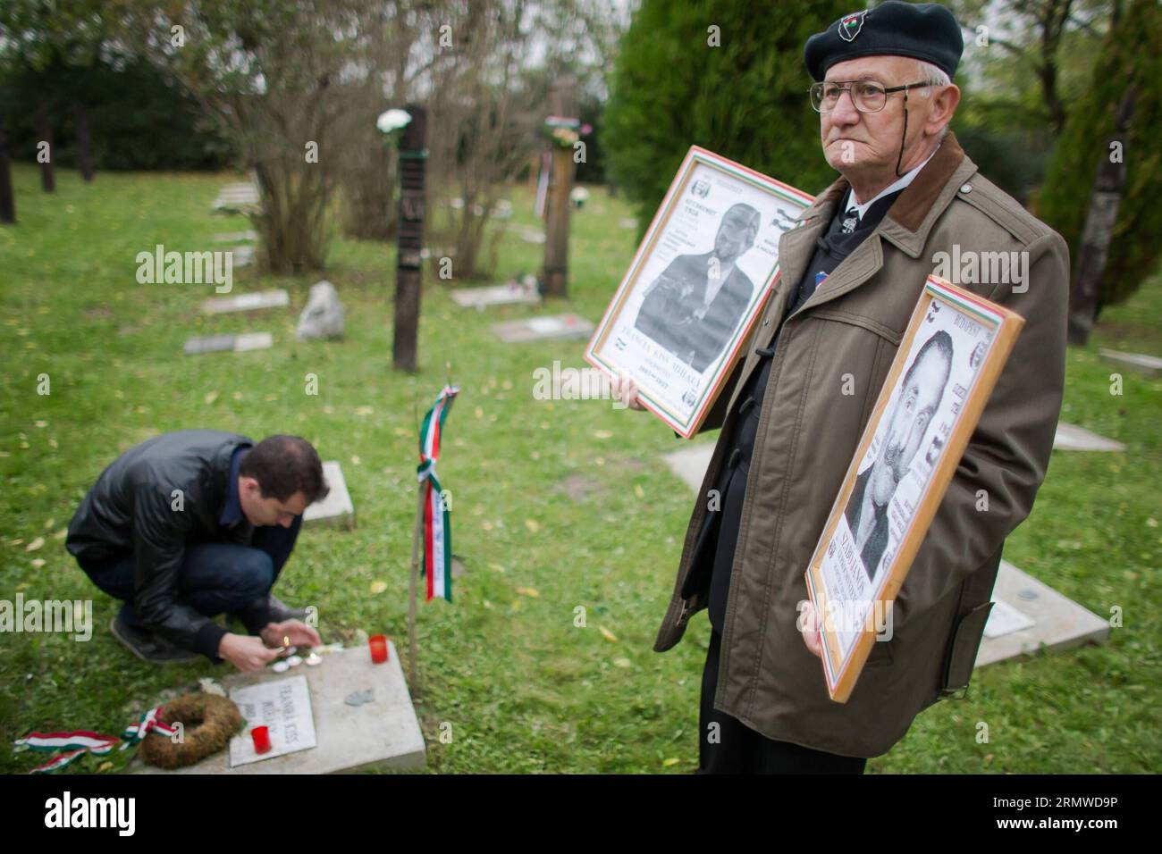 (141023) -- BUDAPEST, Oct. 23, 2014 -- A survivor of the revolution holding portraits stands beside their graves in a cemetery on national holiday commemorating the revolution of 1956 in Budapest, Hungary on Oct. 23, 2014. Hungarians marked Thursday with a series of events remembering the failed 1956 revolution that began on Oct. 23, exactly 58 years ago. ) HUNGARY-BUDAPEST-REVOLUTION-COMMEMORATION AttilaxVolgyi PUBLICATIONxNOTxINxCHN   Budapest OCT 23 2014 a Survivor of The Revolution Holding Portraits stands Beside their Graves in a Cemetery ON National Holiday Commemorating Ting The Revolut Stock Photo