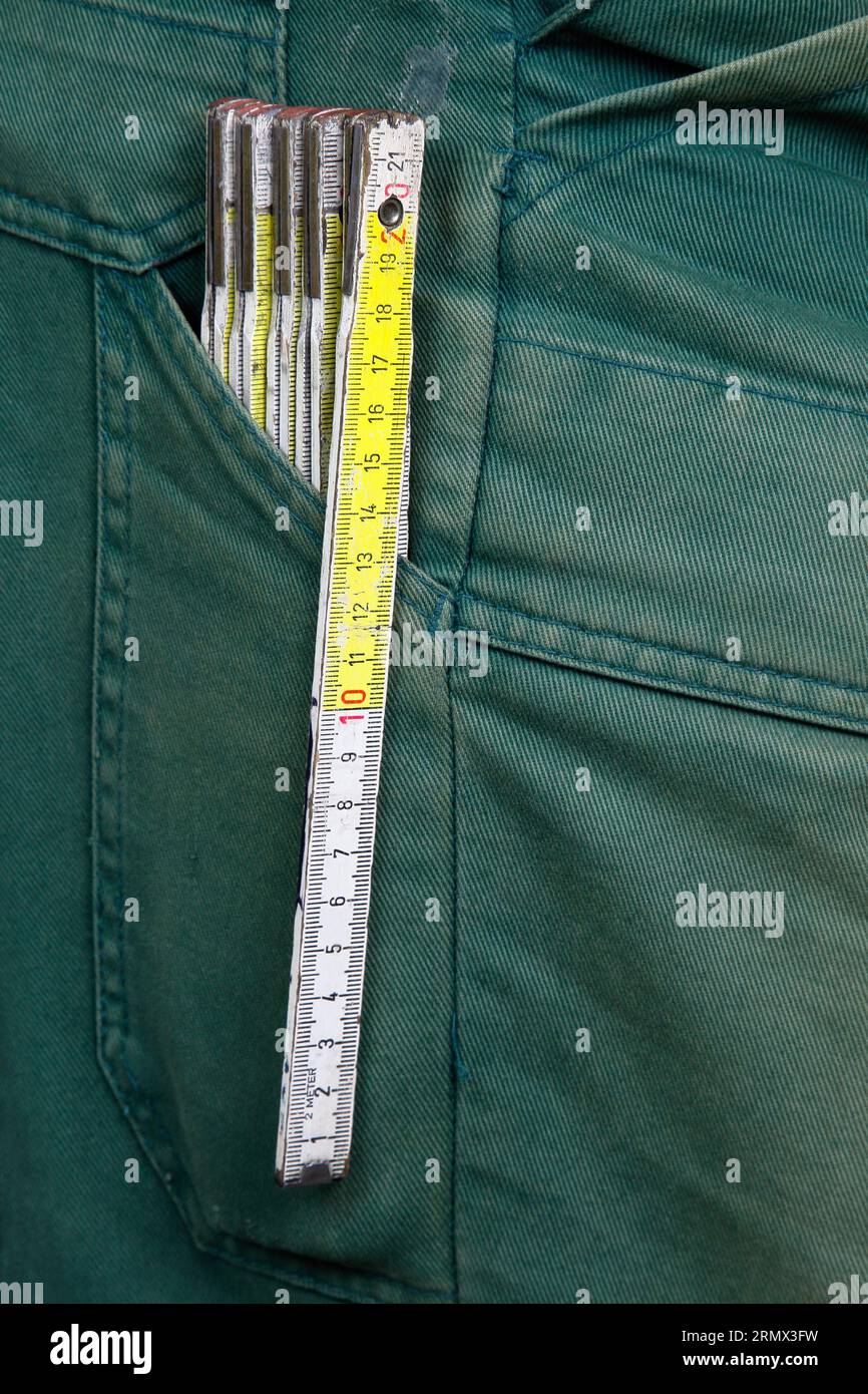 Be moderate. A folding rule made of wood is in the pocket of a pair of green work trousers. Stock Photo