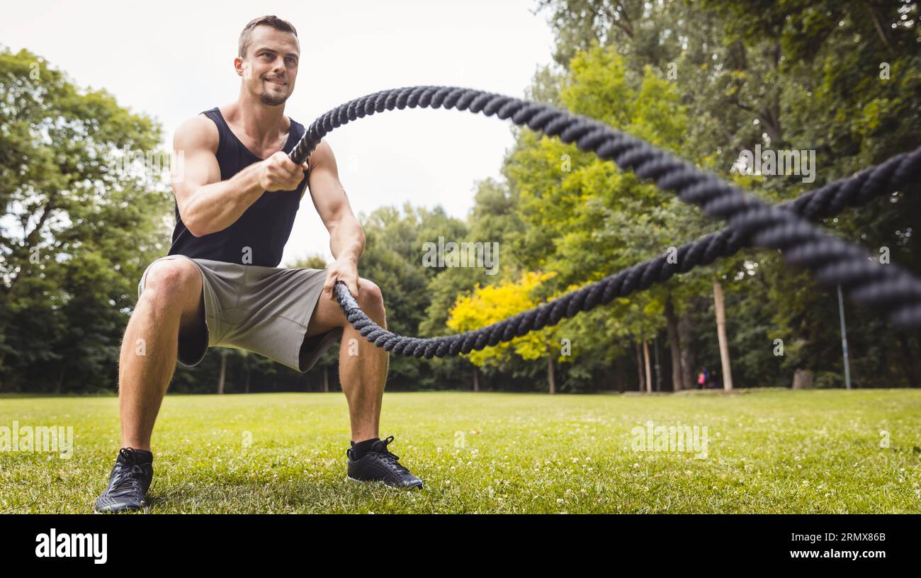 Man in park using battle rope Stock Photo - Alamy