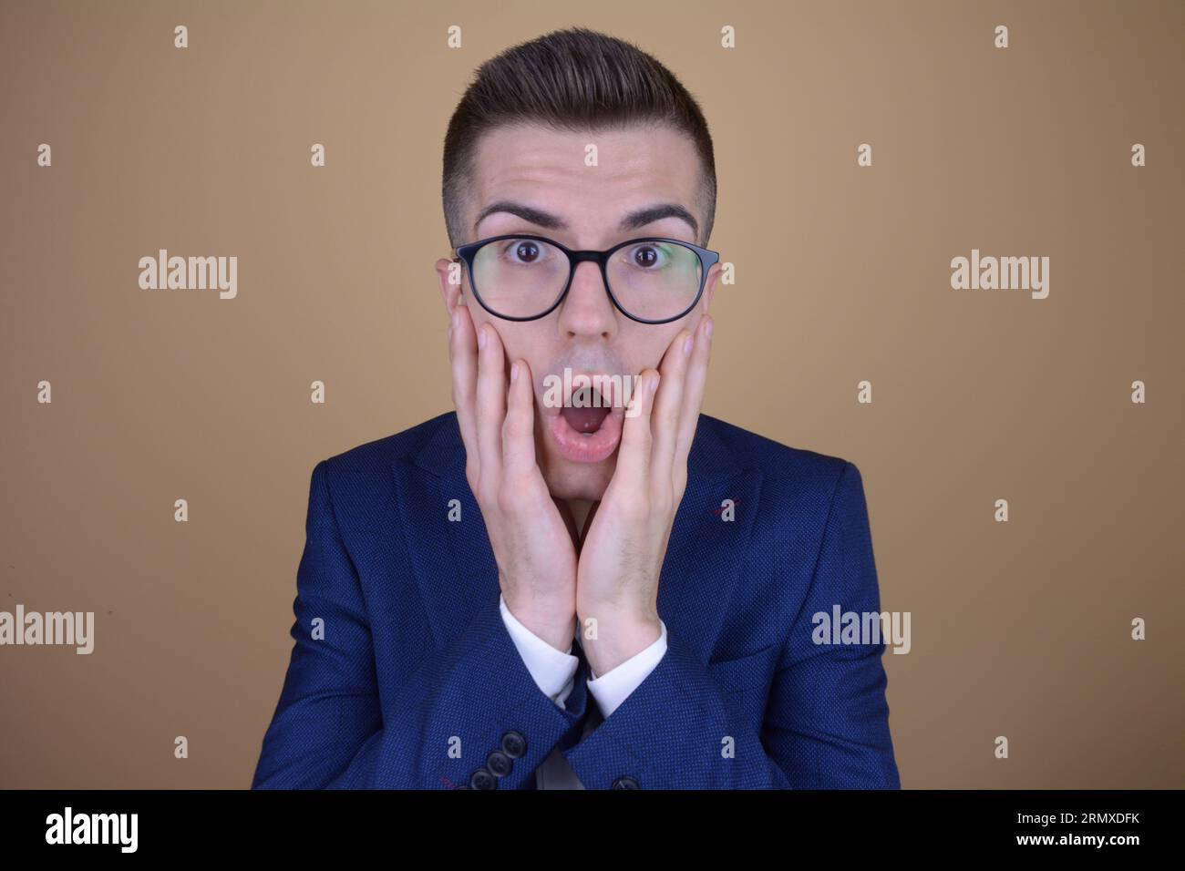 Young Handsome Elegant Man in Shock with Open Mouth Clutching His Cheeks on Isolated Background Stock Photo