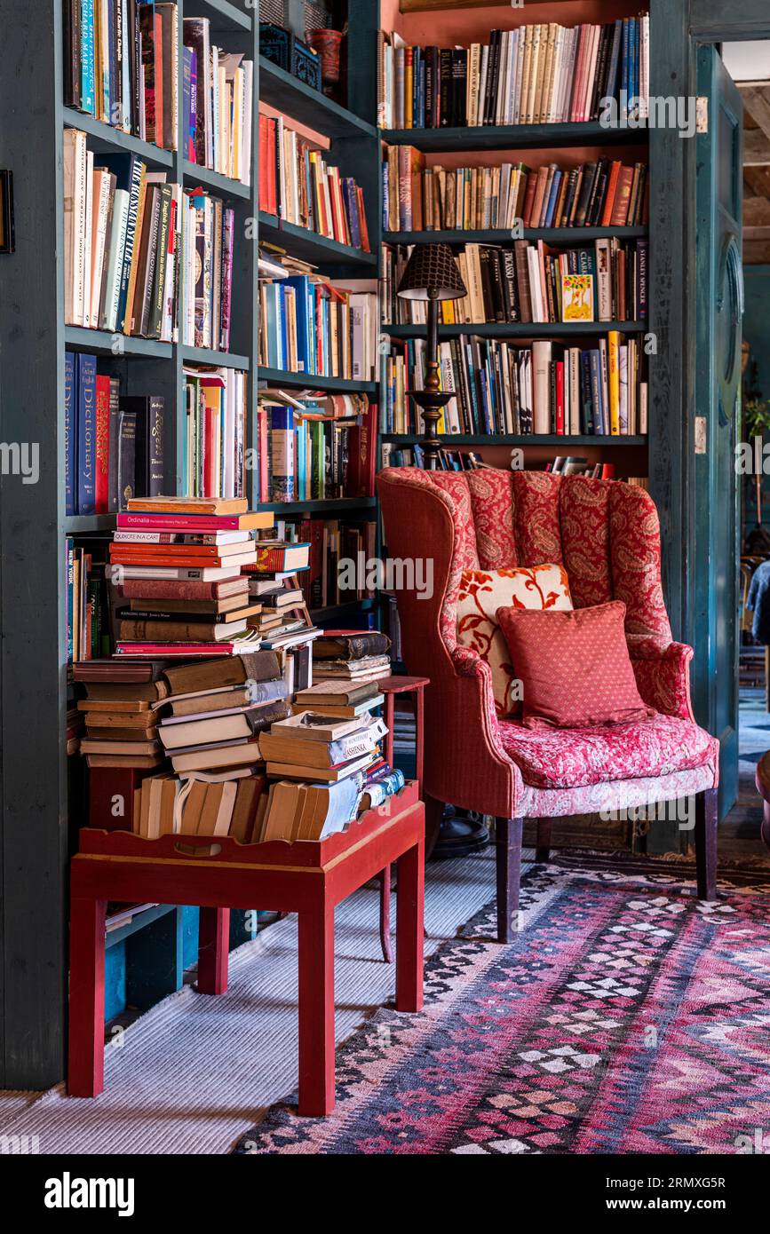 Red armchair and stacked books in 18th century flower loft conversion near Penzance in Cornwall, UK Stock Photo