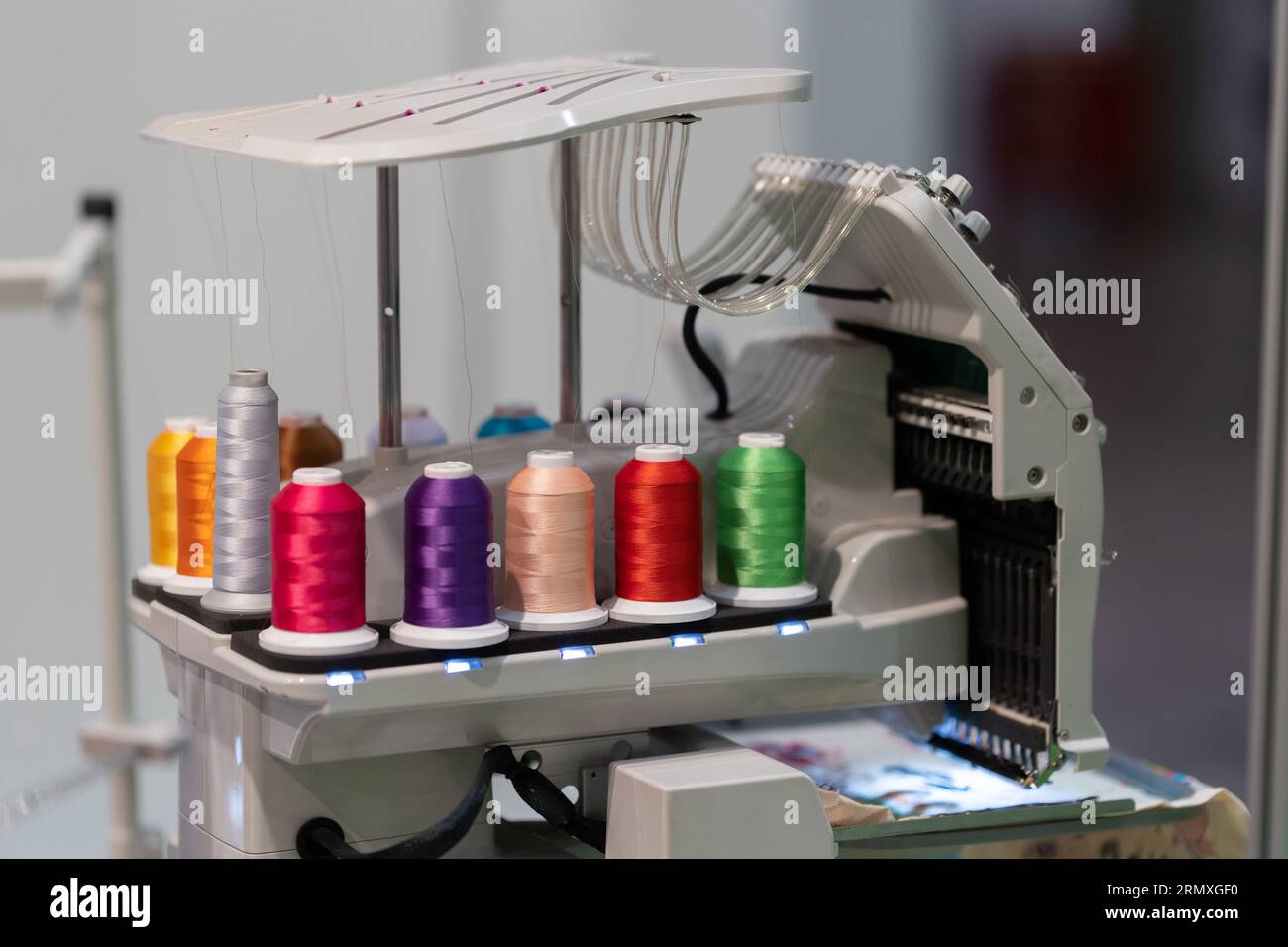 Multi-colored spools of thread are connected to an embroidery machine ...