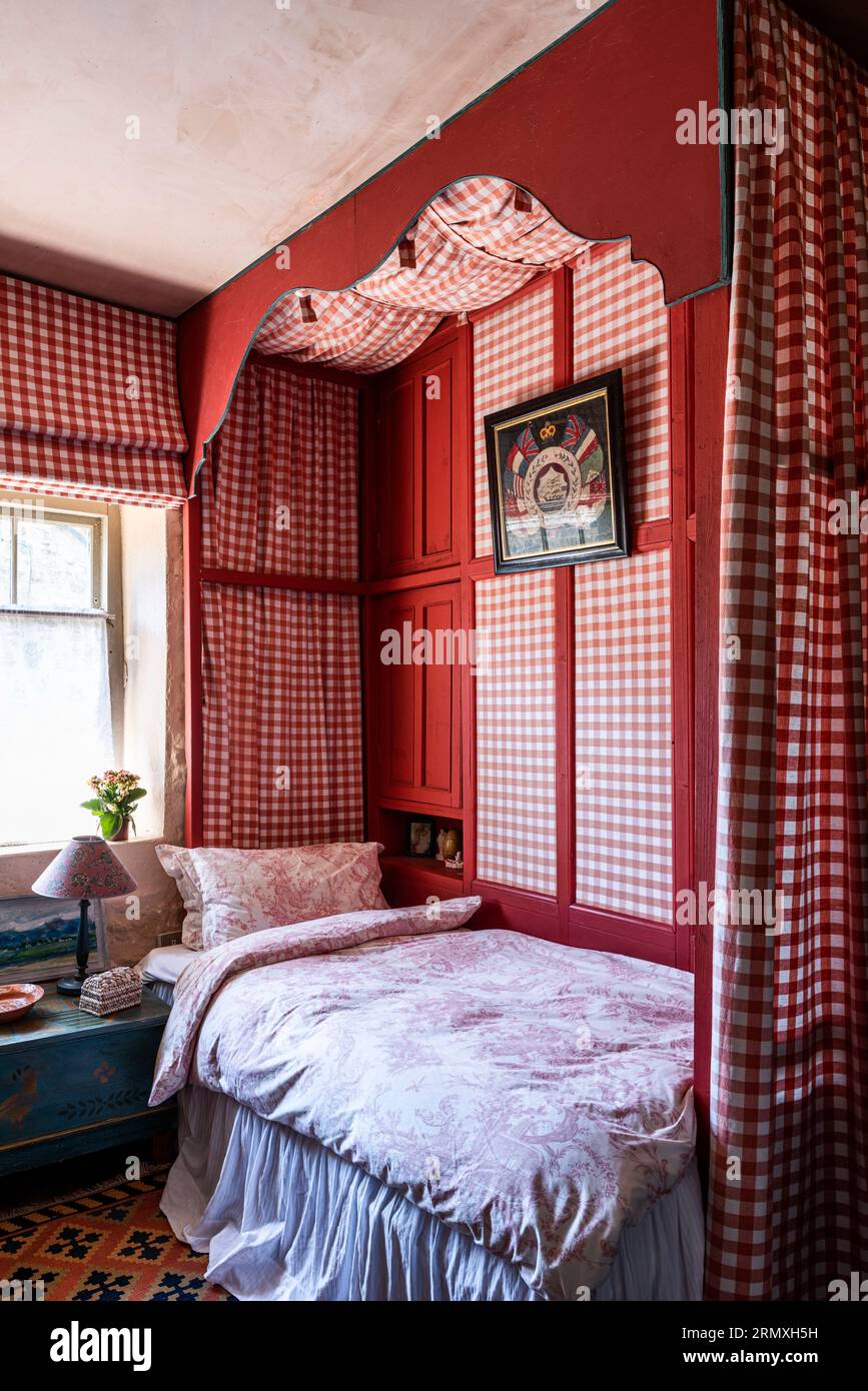 Red gingham fabric surrounds single bed in 18th century flower loft conversion near Penzance in Cornwall, UK Stock Photo