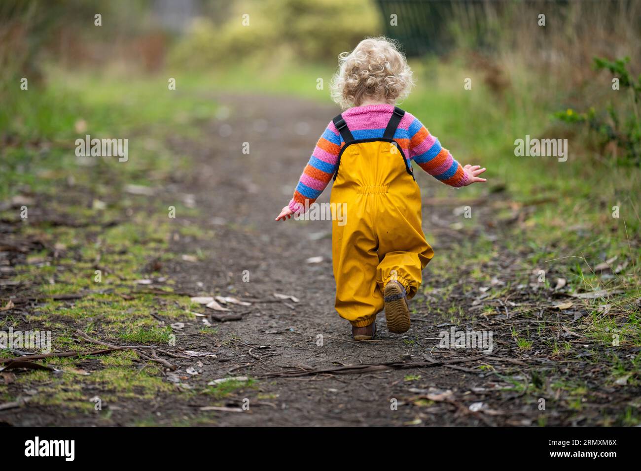 baby running down a path in yellow overalls in the bush Stock Photo - Alamy