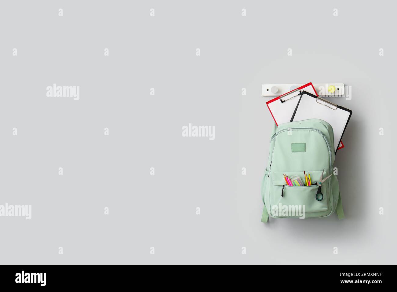 Stylish school backpack with stationery hanging on light wall Stock Photo