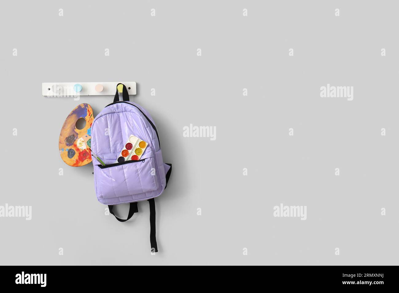 School backpack with paints and brushes hanging on light wall Stock Photo