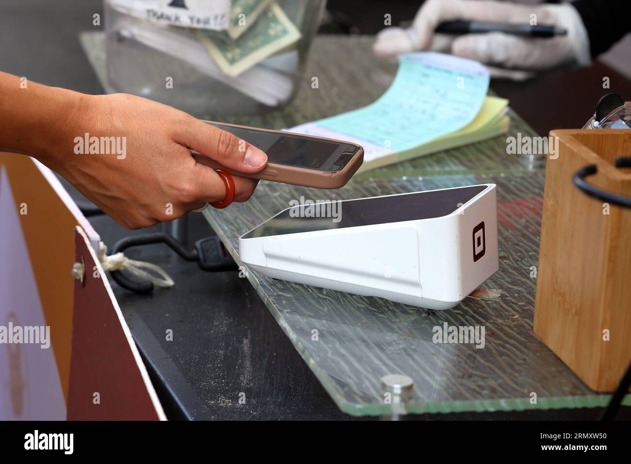 A person holds a smartphone over a wireless Square Terminal point of sales device to transact a NFC mobile payment, or contactless digital payment. Stock Photo