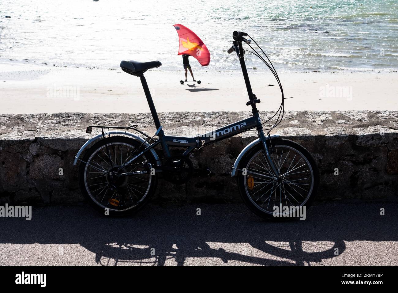 A Moma folding bike with a land windsurfer passing by on a beach in the background Stock Photo