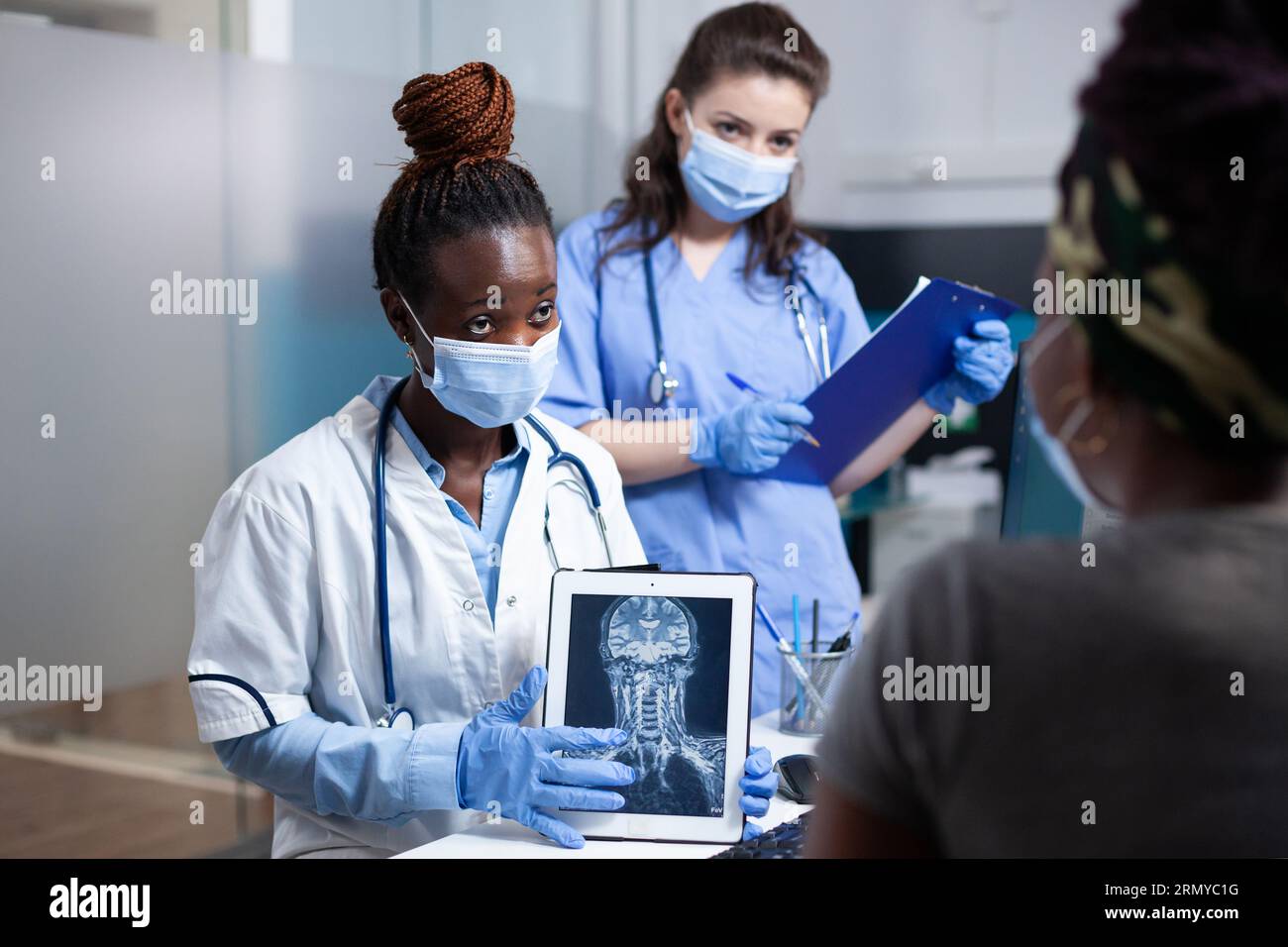 Radiologist and nurse delivering medical exam results to patient using x-ray cervical vertebrae ct scan to diagnose bone injury. Doctor medical checkup visit in sanitary sterile clinic Stock Photo