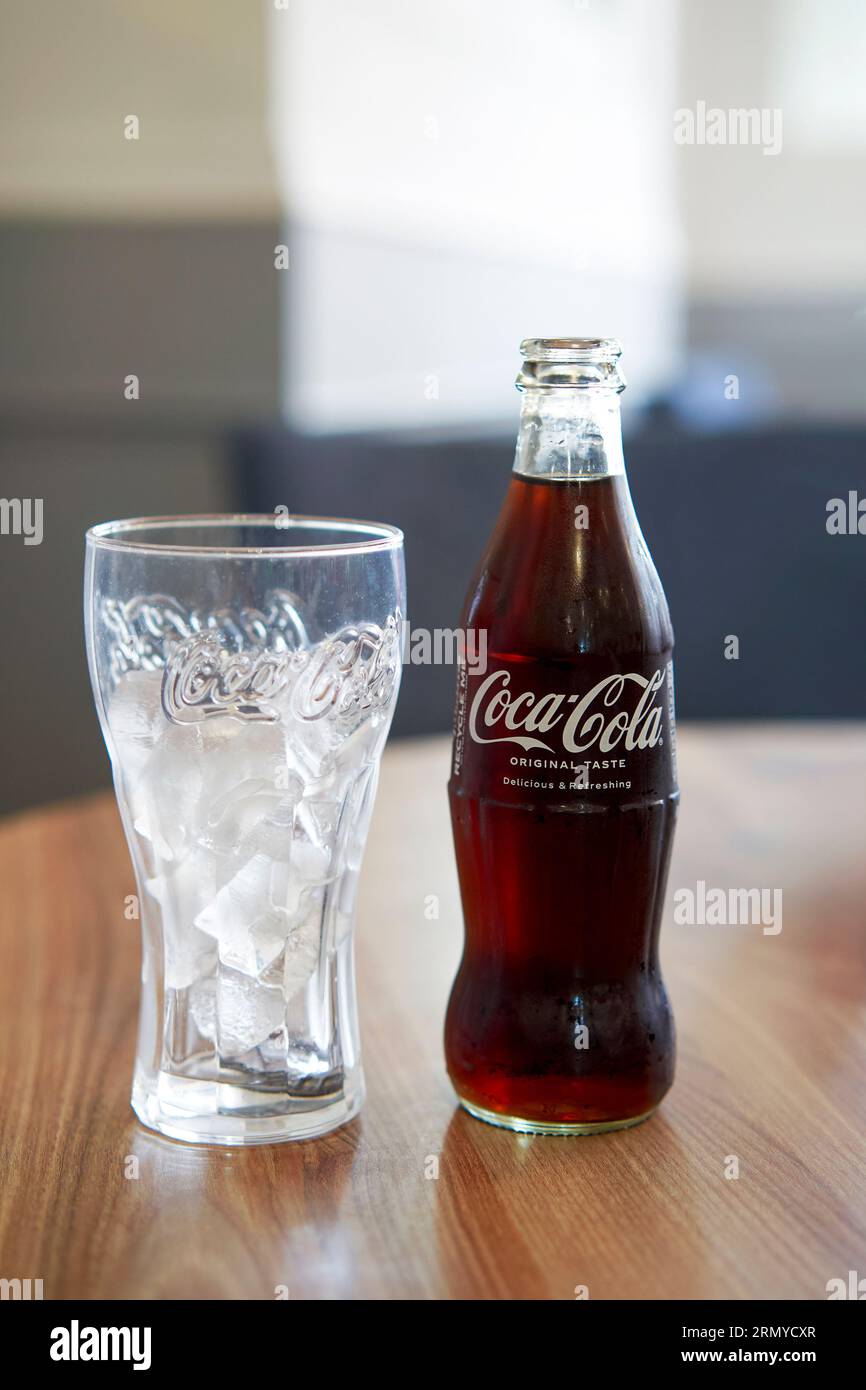 Bottle of Coca Cola on a table with a glass full of ice cubes Stock Photo