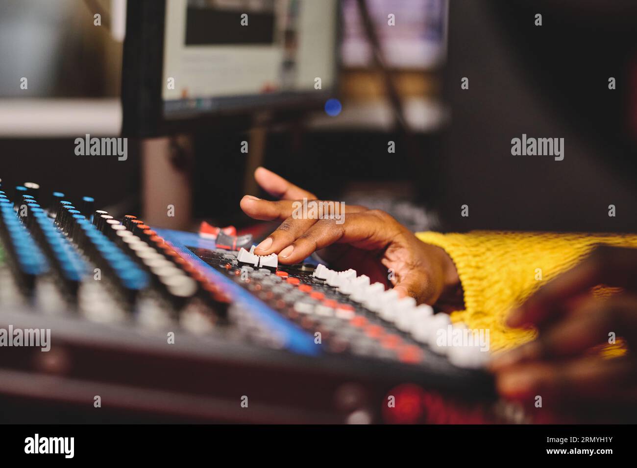 Unrecognizable crop African American woman in yellow sweater using mixing panel with control buttons while working in broadcast studio Stock Photo