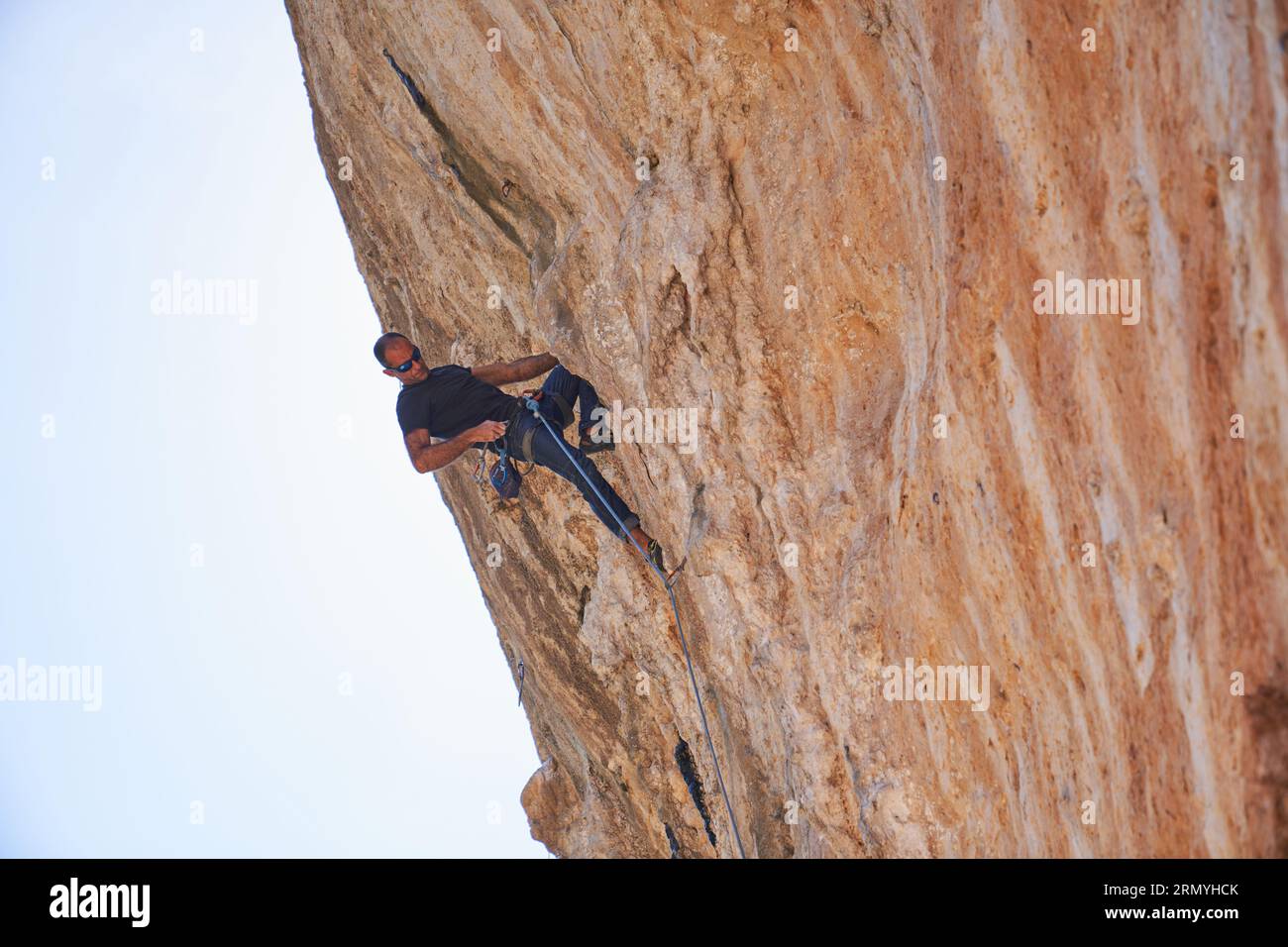 From below full body of male alpinist in safety harness ascending on ...