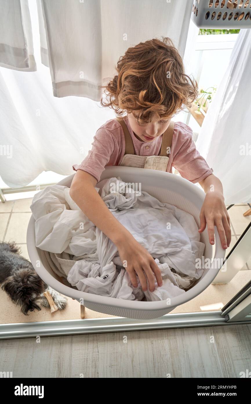 From above of focused kid hanging up white sheets on clothesline while doing household routine on balcony at home Stock Photo