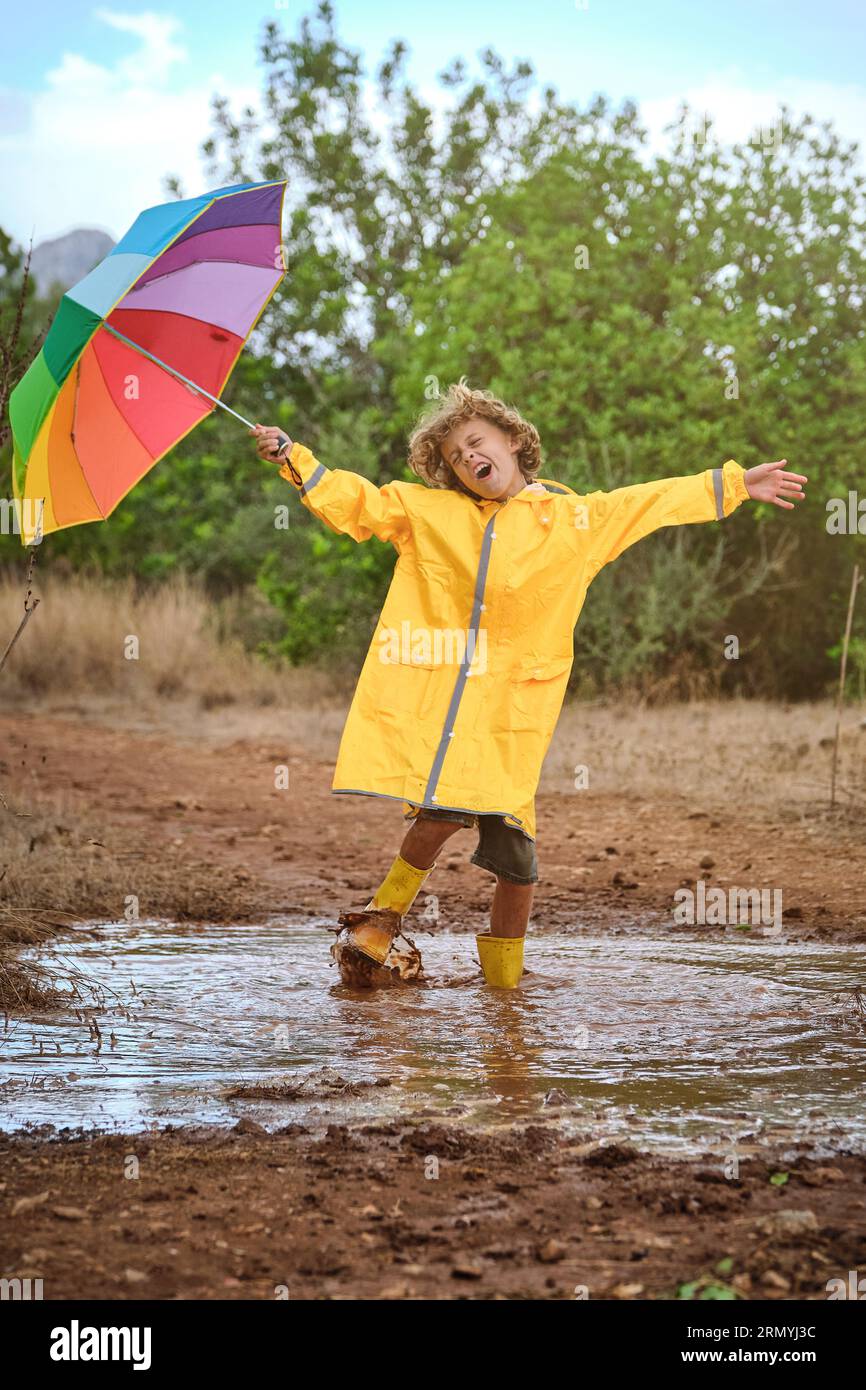 Side view of cute little boy in yellow raincoat and rubber boots