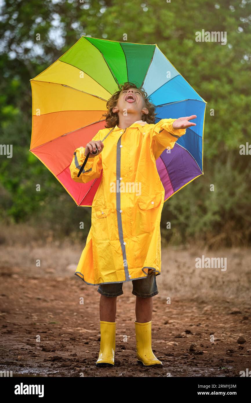 Full body of little boy in yellow raincoat and rubber boots with