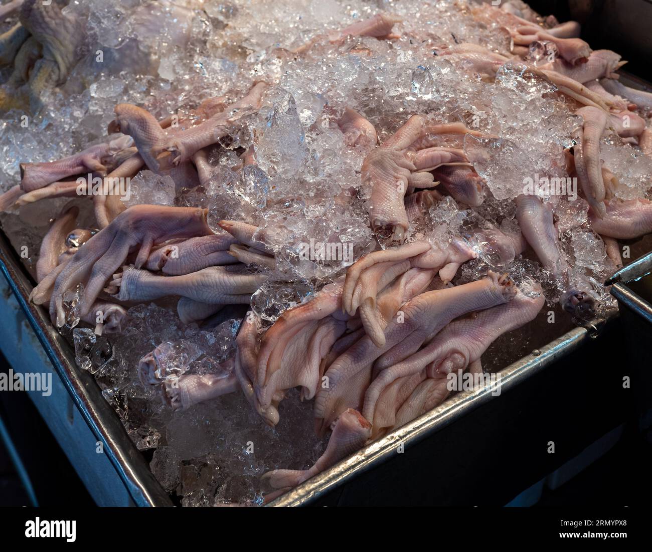 A large crate of delectable chicken feet rests on ice at a vibrant street market in Bangkok, Thailand. Stock Photo