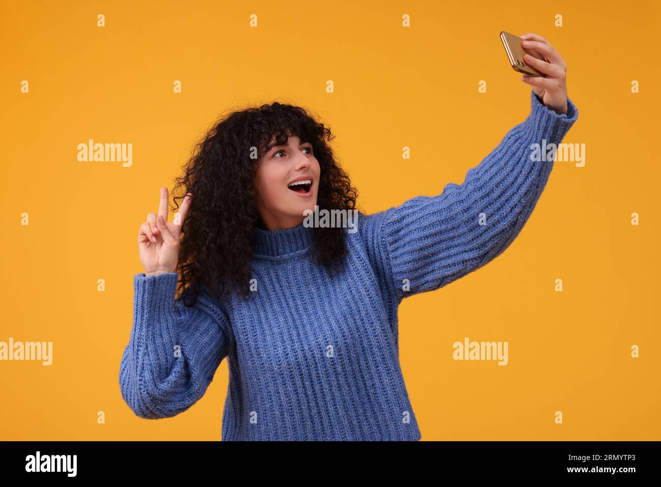 Beautiful young woman taking selfie with smartphone on orange ...
