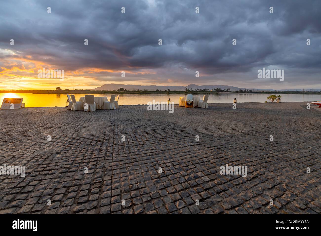 View from a riverfront resort with tables facing the water along the Nile River under colorful twilight skies in Luxor, Egypt. Stock Photo