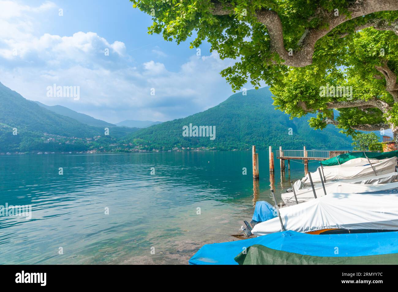 Covered boats pulled up on shore of Lake Lugano surrounded by mountains
