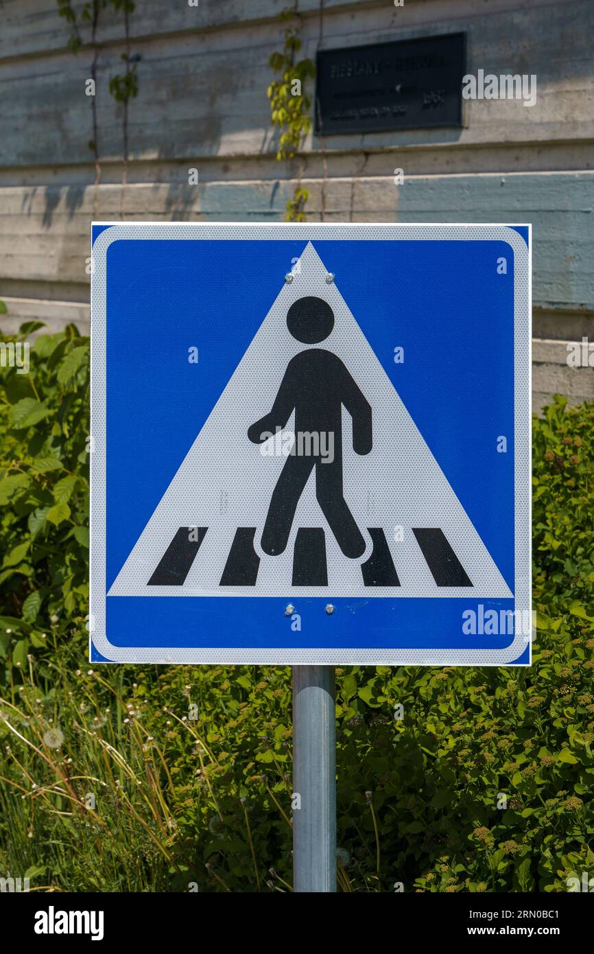 Pedestrian crossing sign in summer with green bushes and a concrete wall in the background Stock Photo