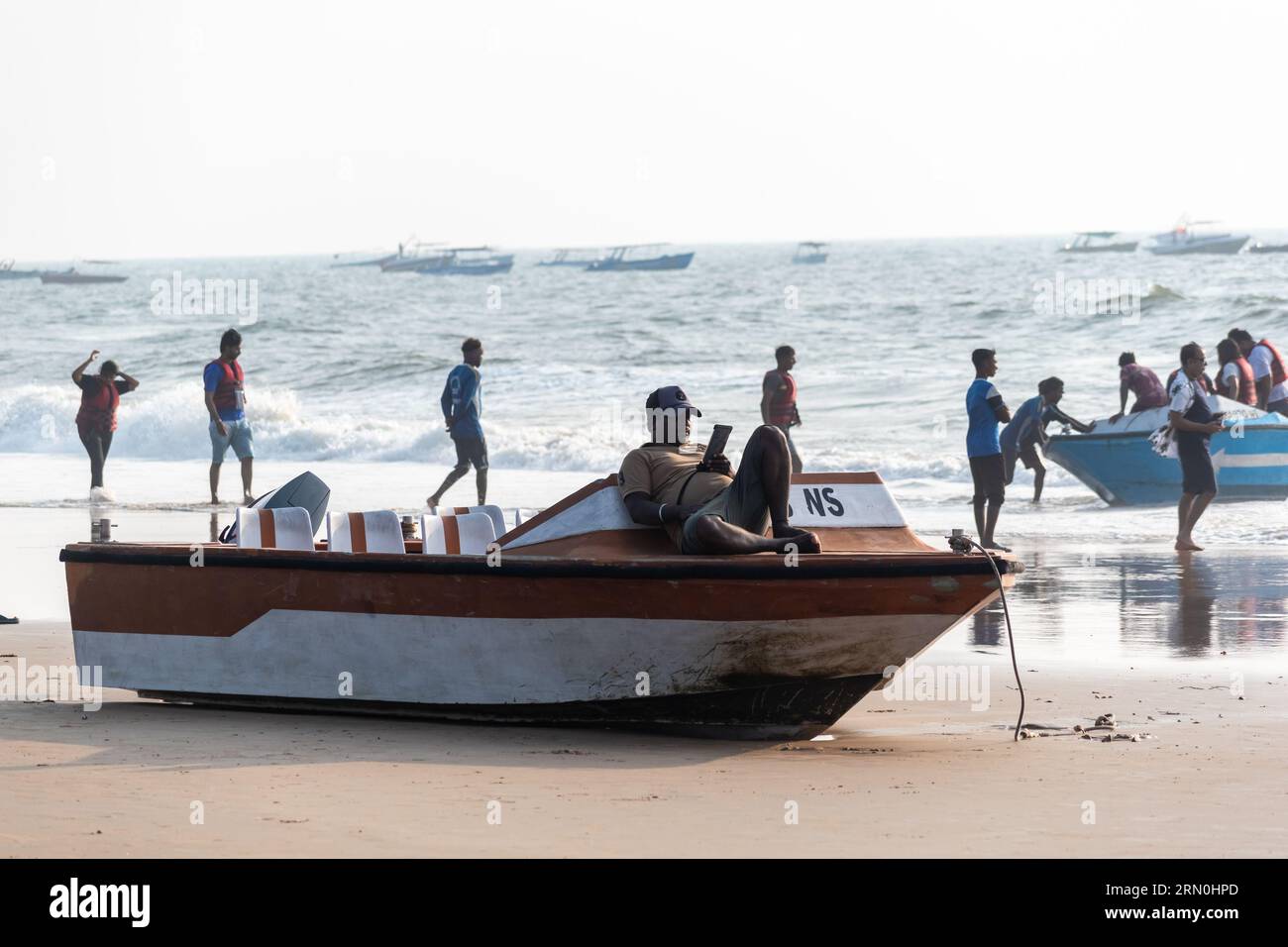 Calangute, Goa, India - January 2023: An Indian fisherman lying on his boat on a crowded beach in Goa. Stock Photo