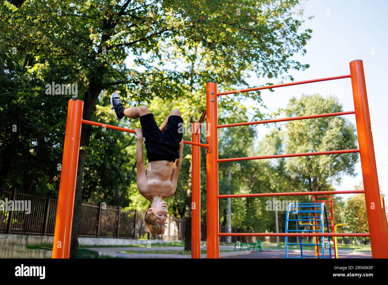 Going in for sports boy hanging upside down. Street workout on a horizontal bar in the school park. Stock Photo