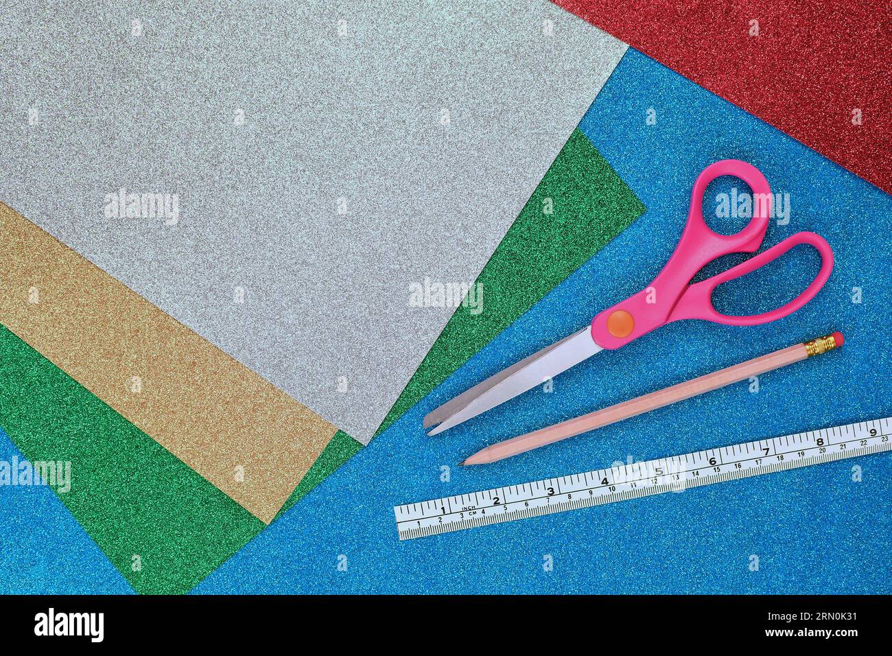 A flat, top view of an Arts and Crafts background with colourful, sparkly, glitter paper, scissors, pencil and ruler with copy space Stock Photo