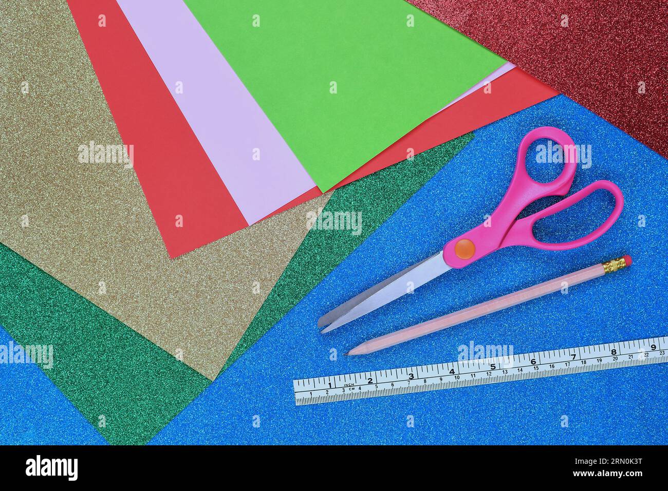 A flat, top view of an Arts and Crafts background with coloured cardboard, sparkly, glitter paper, scissors, pencil and ruler with copy space Stock Photo