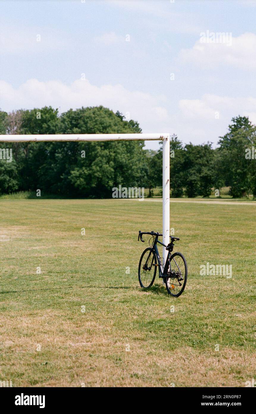 A racing bike leaning against a goal post in the middle of a green football field in park Stock Photo