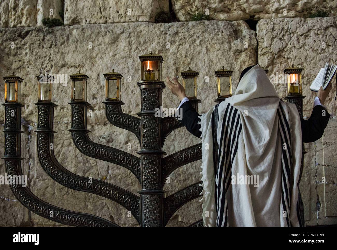 JERUSALEM, Dec. 16, 2014 -- An Ultra-Orthodox Jewish man prays to mark Hanukkah in front of a large-sized Hannukiya at the Western Wall in the Old City of Jerusalem, on Dec. 16, 2014. Hanukkah, also known as the Festival of Lights and Feast of Dedication, is an eight-day Jewish holiday commemorating the rededication of the Holy Temple (the Second Temple) in Jerusalem at the time of the Maccabean Revolt against the Seleucid Empire of the 2nd Century B.C. Hanukkah is observed for eight nights and days, starting on the 25th day of Kislev according to the Hebrew calendar, which may occur at any ti Stock Photo