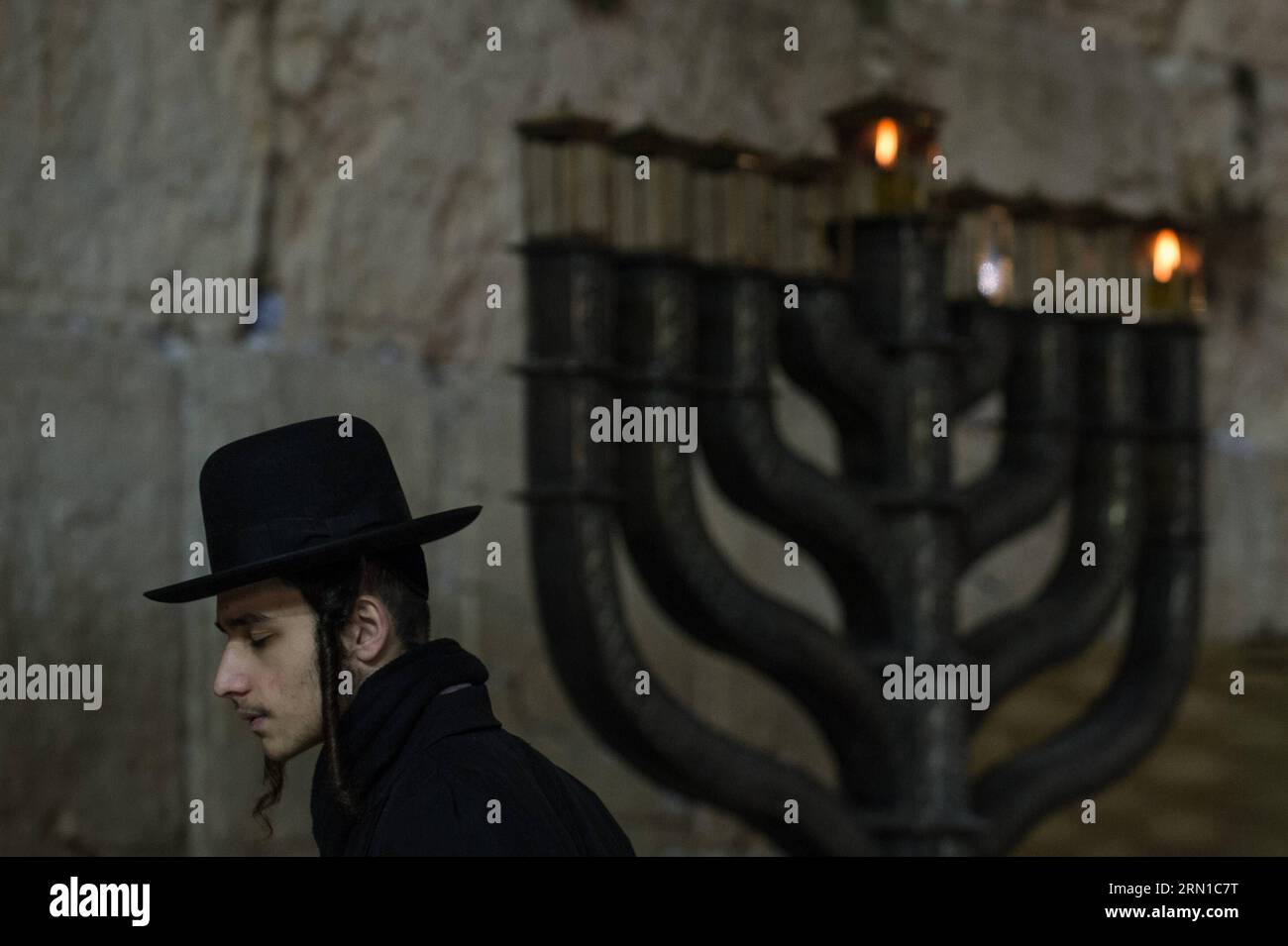 JERUSALEM, Dec. 16, 2014 -- An Ultra-Orthodox Jewish man prays to mark Hanukkah in front of a large-sized Hannukiya at the Western Wall in the Old City of Jerusalem, on Dec. 16, 2014. Hanukkah, also known as the Festival of Lights and Feast of Dedication, is an eight-day Jewish holiday commemorating the rededication of the Holy Temple (the Second Temple) in Jerusalem at the time of the Maccabean Revolt against the Seleucid Empire of the 2nd Century B.C. Hanukkah is observed for eight nights and days, starting on the 25th day of Kislev according to the Hebrew calendar, which may occur at any ti Stock Photo