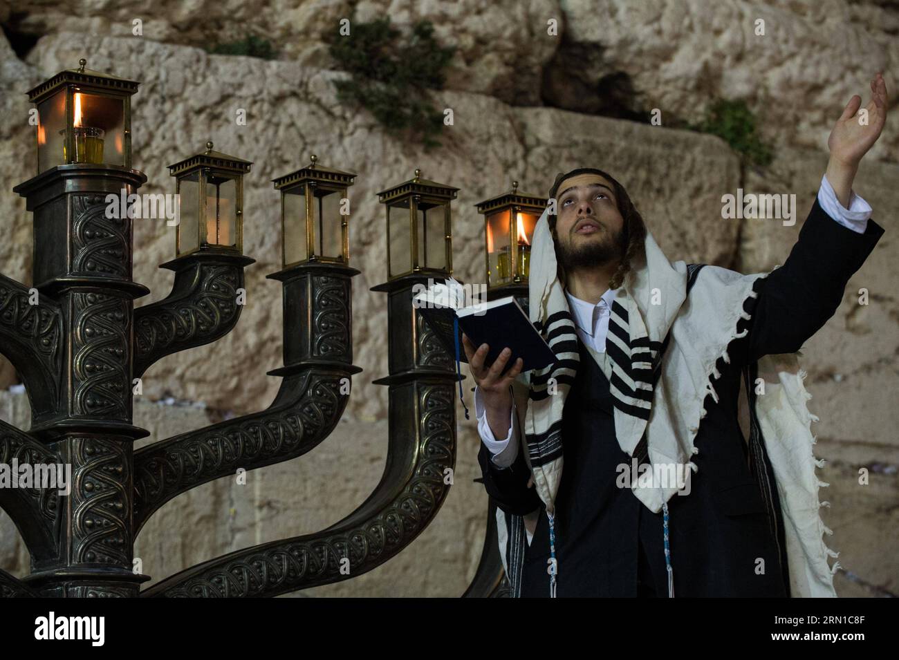 JERUSALEM, Dec. 16, 2014 -- An Ultra-Orthodox Jewish man prays to mark Hanukkah in front of a large-sized Hannukiya at the Western Wall in the Old City of Jerusalem, on Dec. 16, 2014. Hanukkah, also known as the Festival of Lights and Feast of Dedication, is an eight-day Jewish holiday commemorating the rededication of the Holy Temple (the Second Temple) in Jerusalem at the time of the Maccabean Revolt against the Seleucid Empire of the 2nd Century B.C. Hanukkah is observed for eight nights and days, starting on the 25th day of Kislev according to the Hebrew calendar, which may occur at any ti Stock Photo