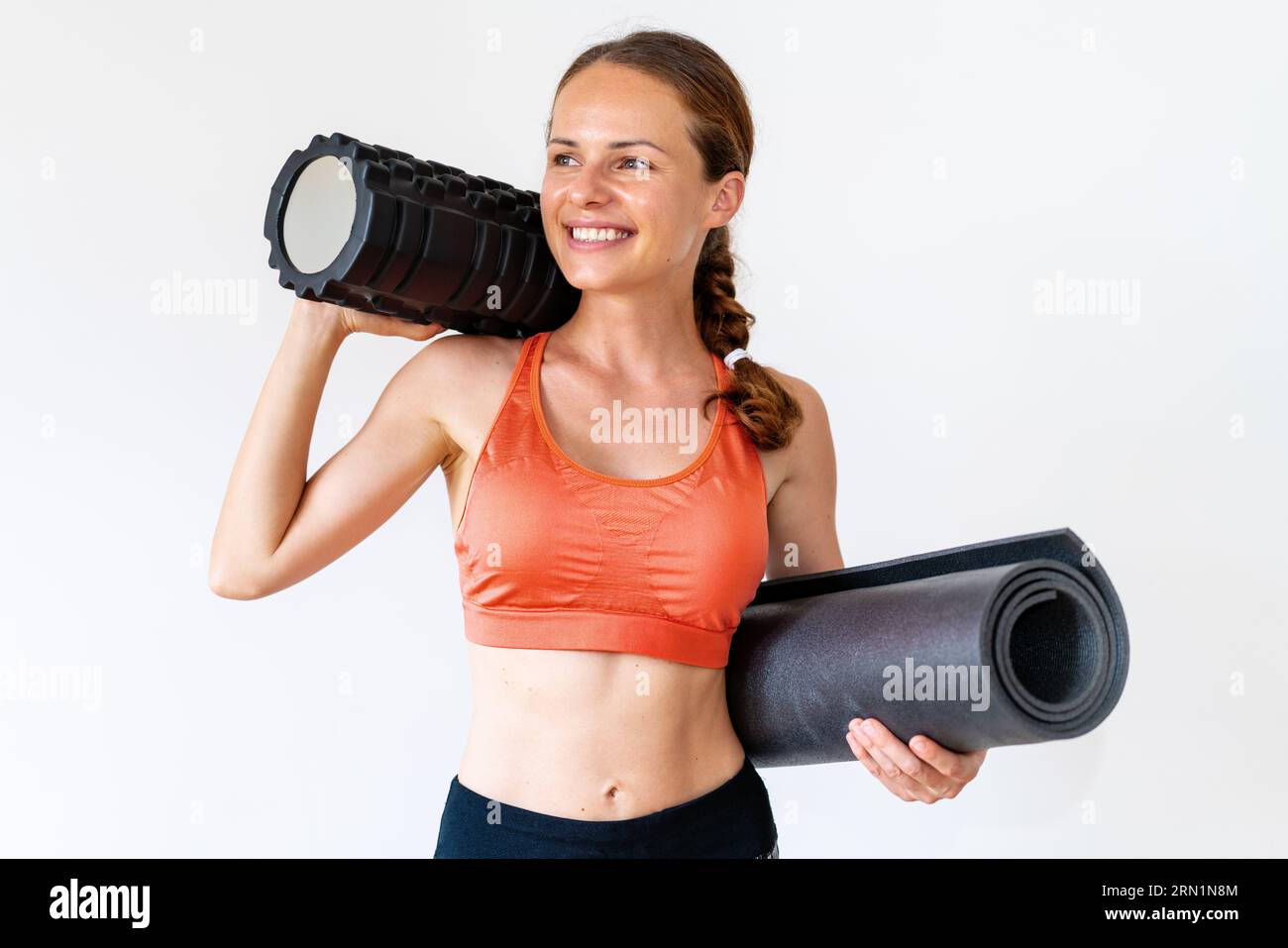 Young athlete slim woman in sportswear holding foam roller and rolled ...