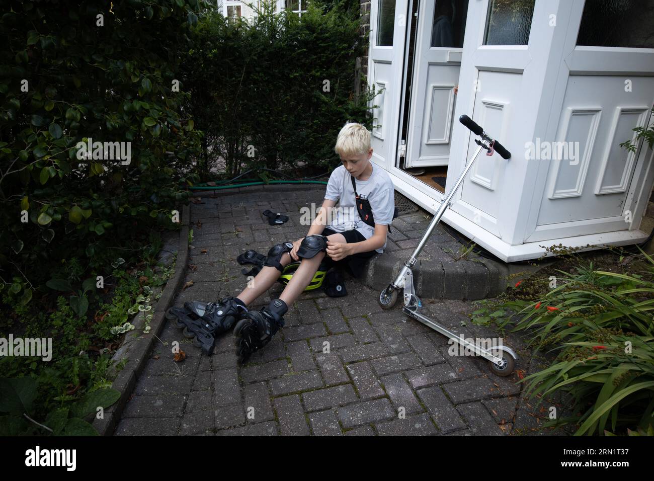 12 year-old boy outside his residential home putting on his roller blades, England, United Kingdom Stock Photo