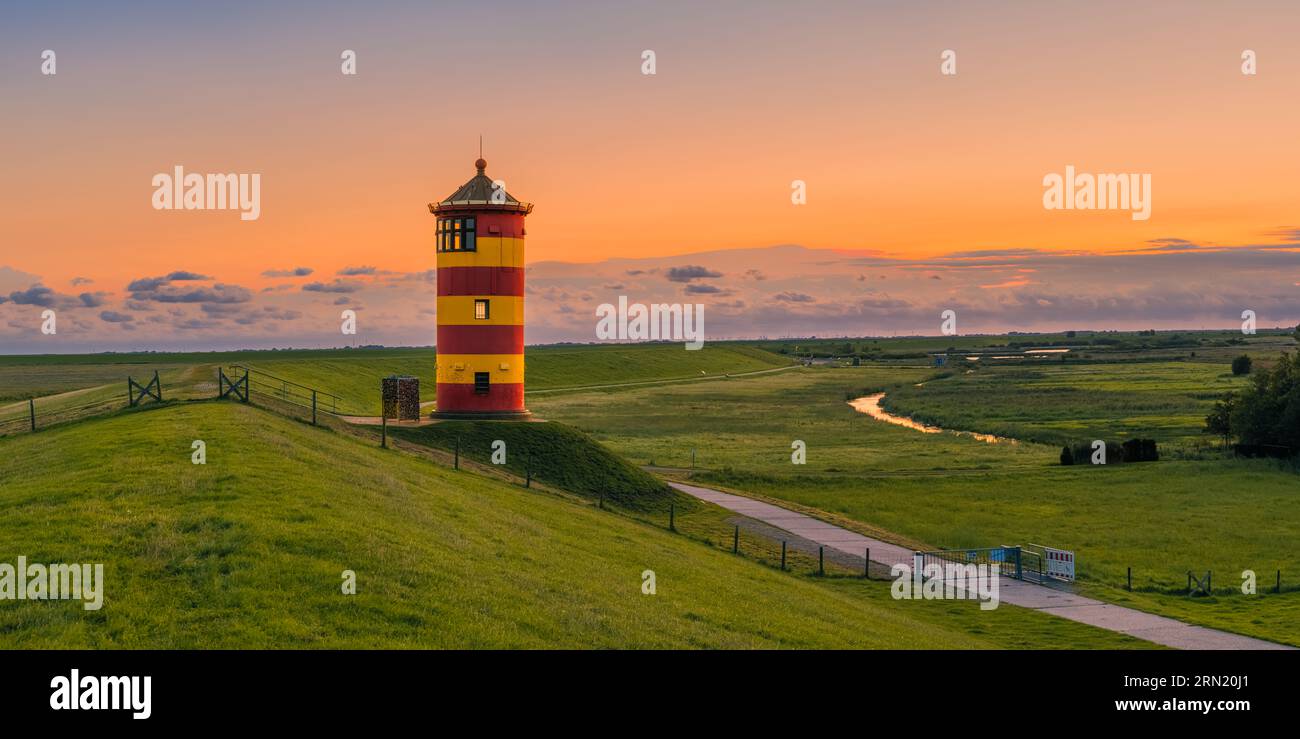 A wide 2:1 panorama image of a sunrise at the lighthouse of Pilsum, located between Pilsum and Greetsiel on the North Sea dike that belongs to the mun Stock Photo