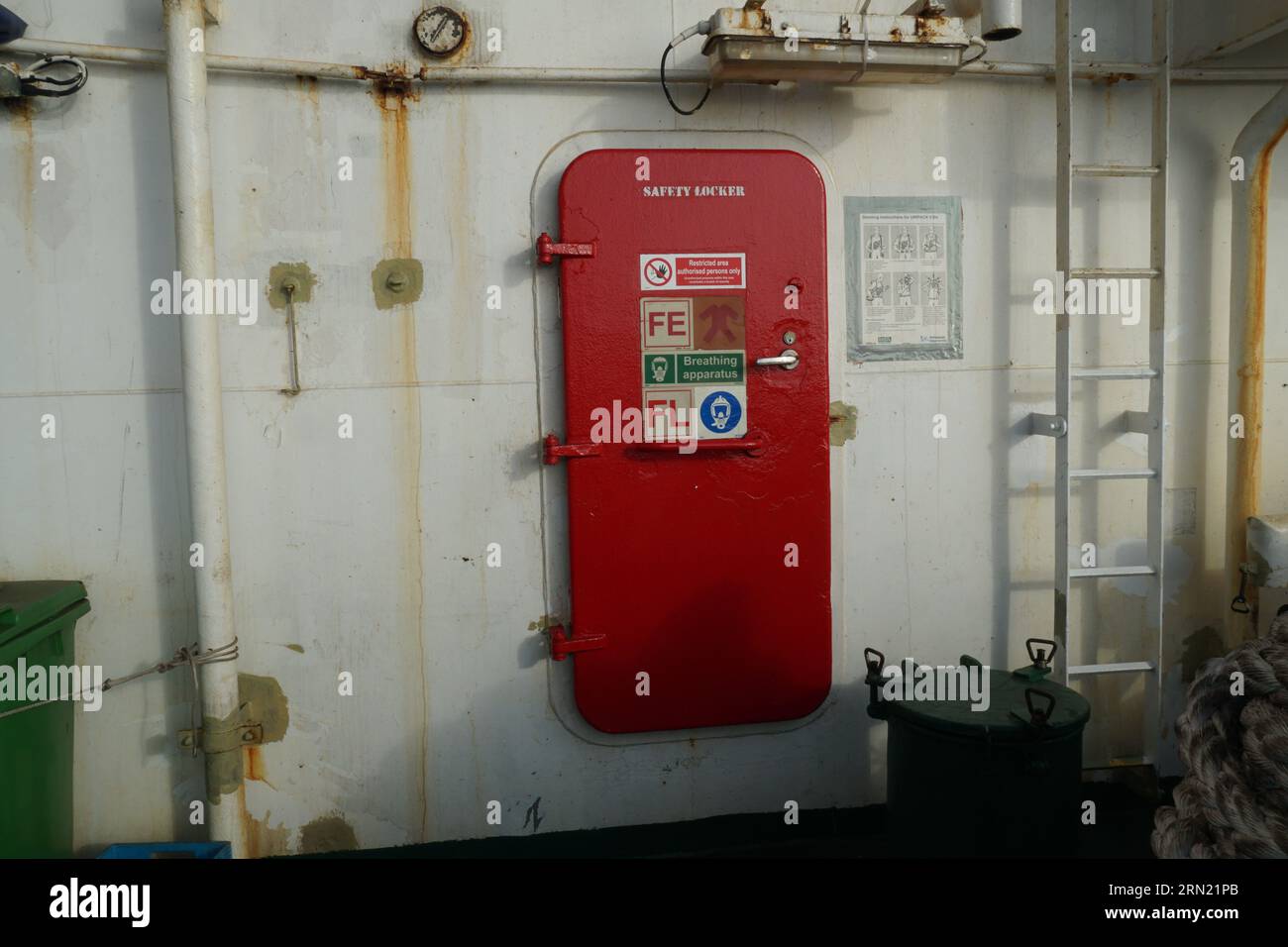 Red metal door with stickers is closing the entrance to safety locker on the container vessel. Stock Photo