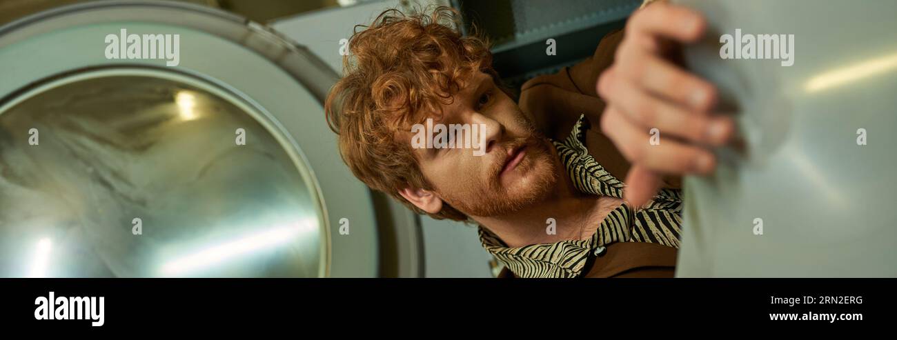 fashionable young man posing in washing machine in public laundry, banner Stock Photo