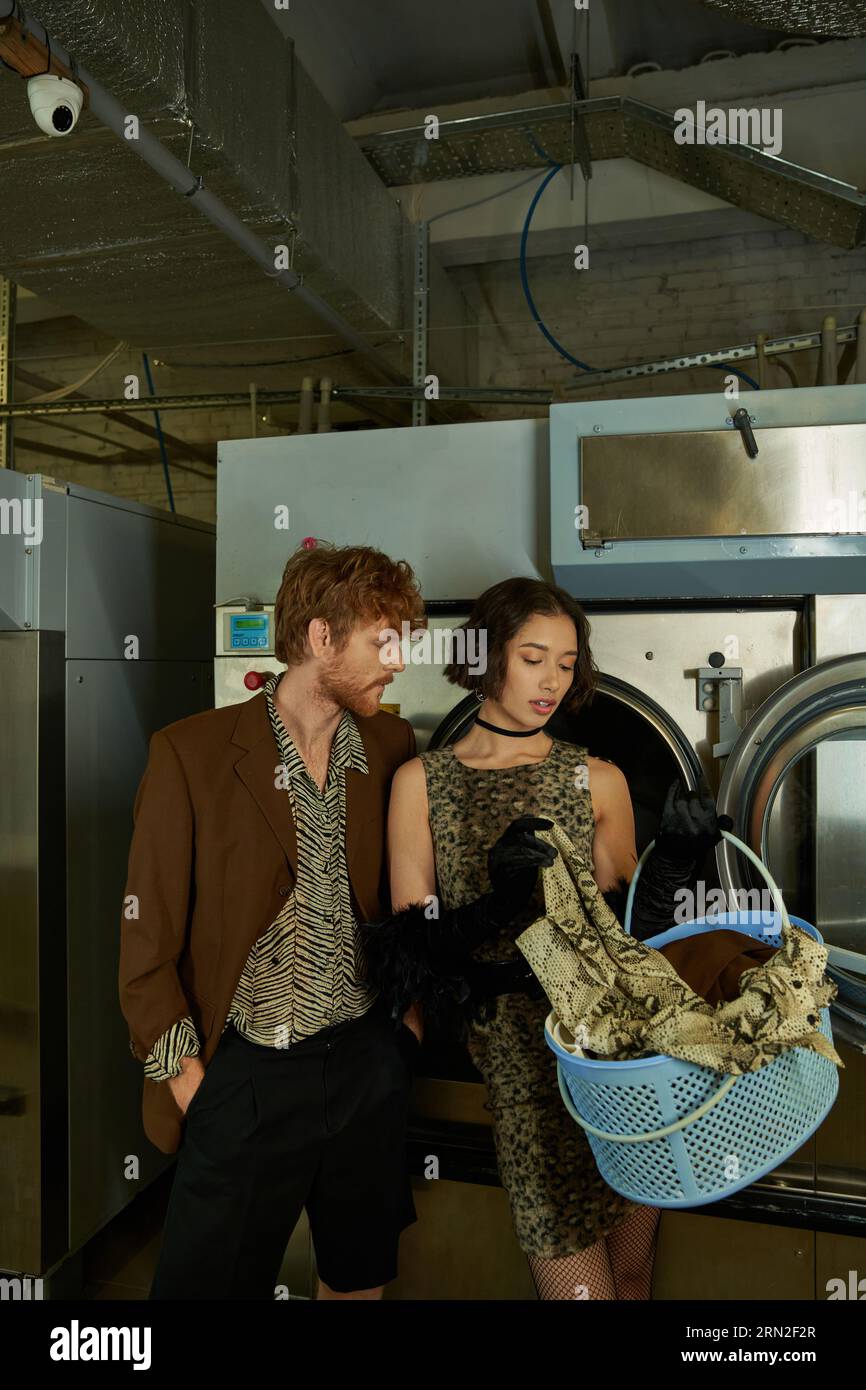 stylish young asian woman holding basket with clothes near boyfriend in public laundry Stock Photo
