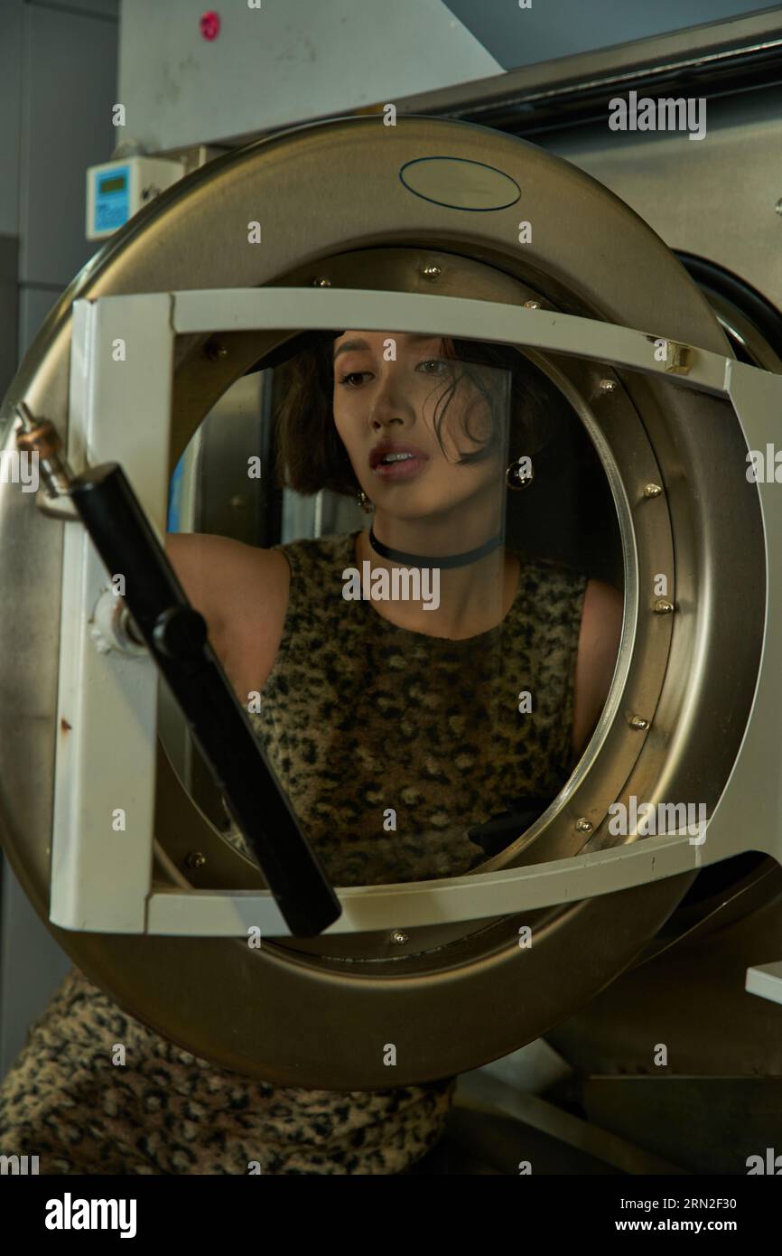 elegant young asian woman posing behind door of washing machine in public laundry Stock Photo