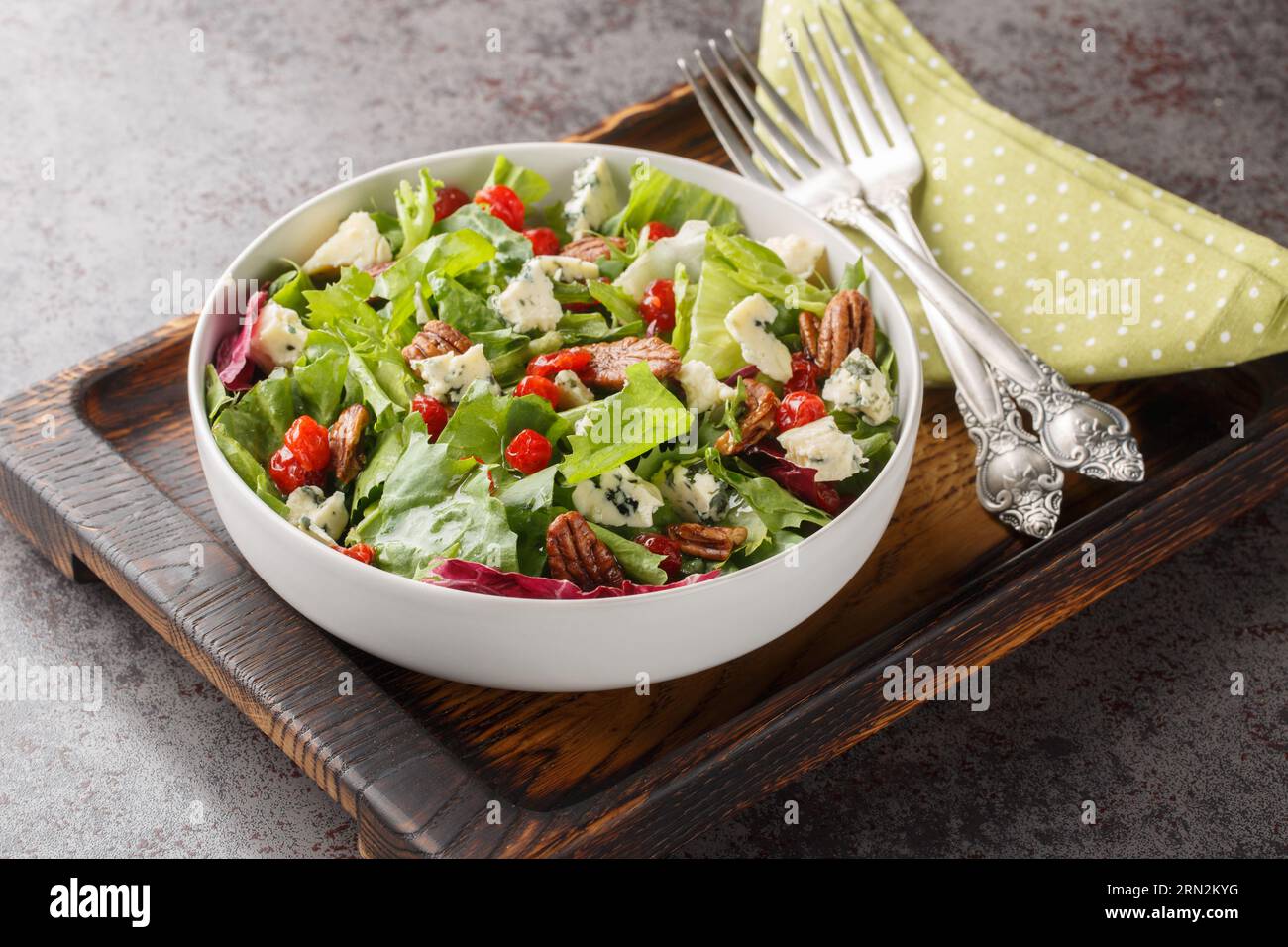 Delicious fresh salad with leaf lettuce, dried cherries, gorgonzola cheese, pecans dressed with vinaigrette sauce close-up in a bowl on the table. Hor Stock Photo