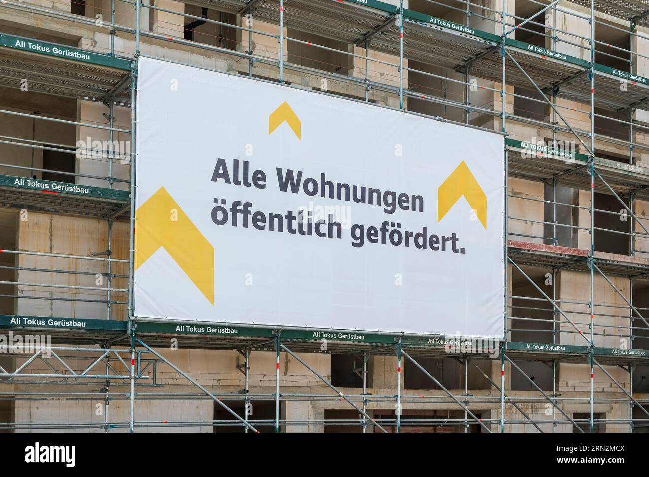 Construction site where flats are being built with scaffolding on which a banner hangs indicating that the flats are publicly funded. Stock Photo