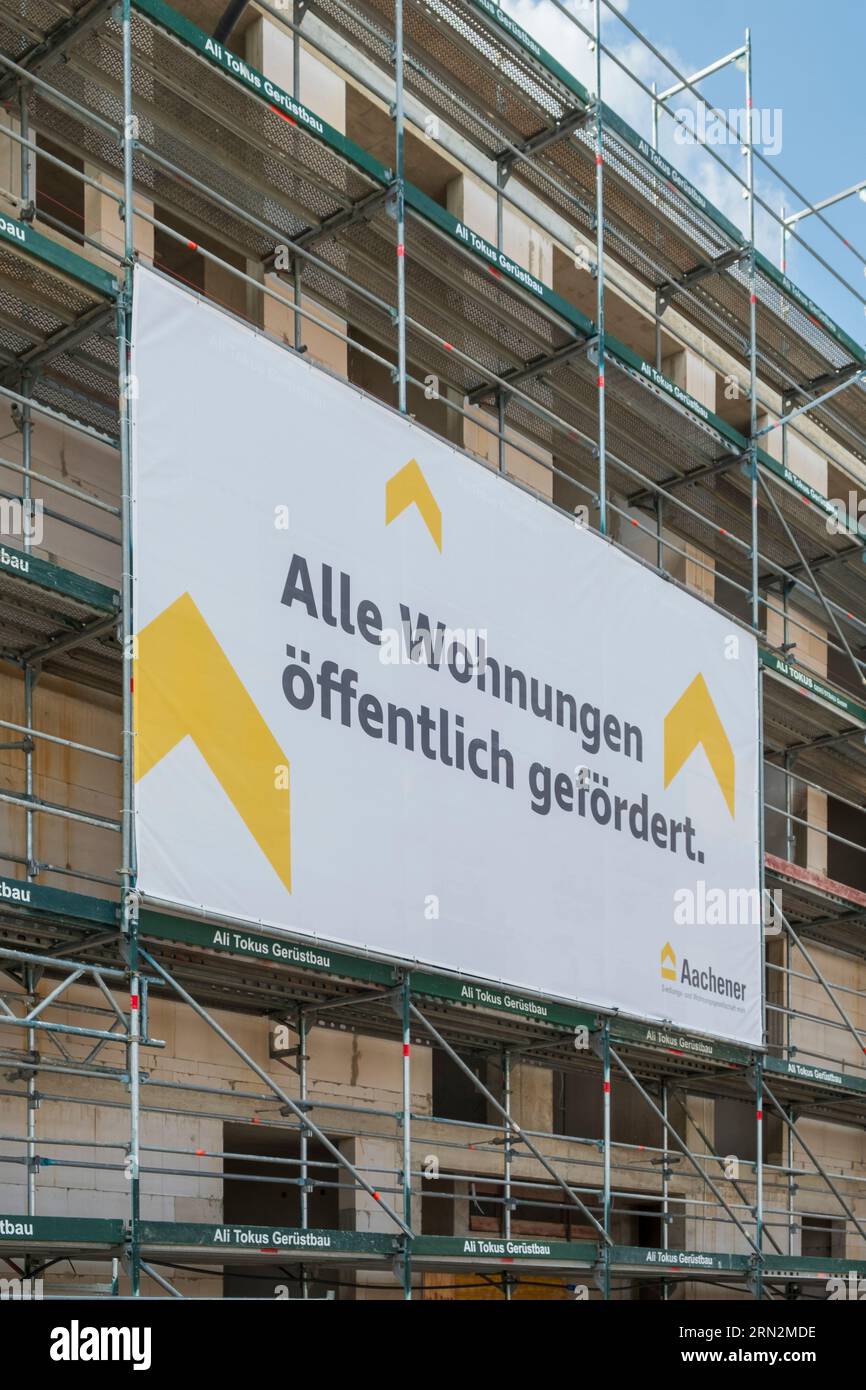 Construction site where flats are being built with scaffolding on which a banner hangs indicating that the flats are publicly funded. Stock Photo